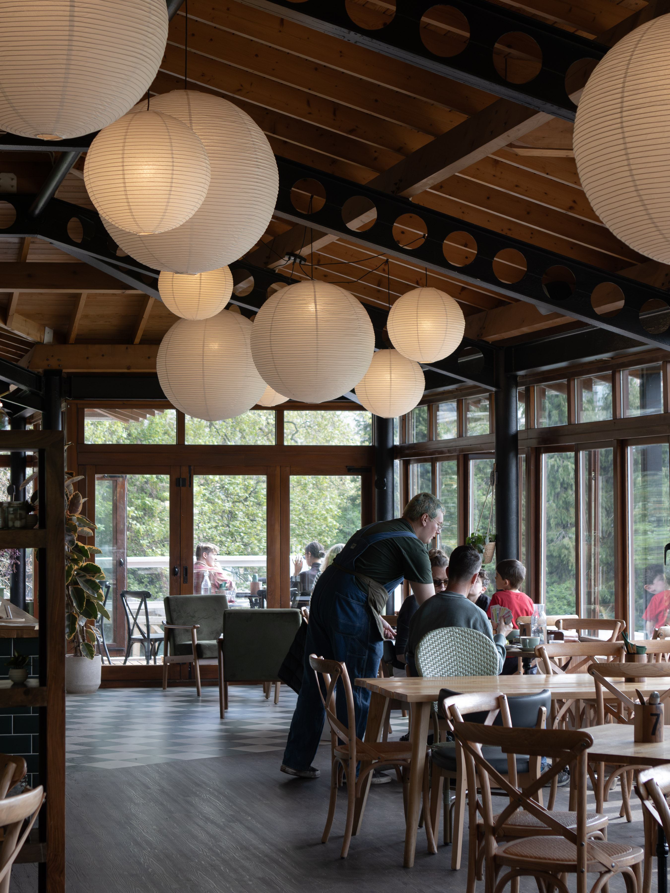 Sunny restaurant interior with paper-lantern lights, timber roof and waiter taking an order at a family table