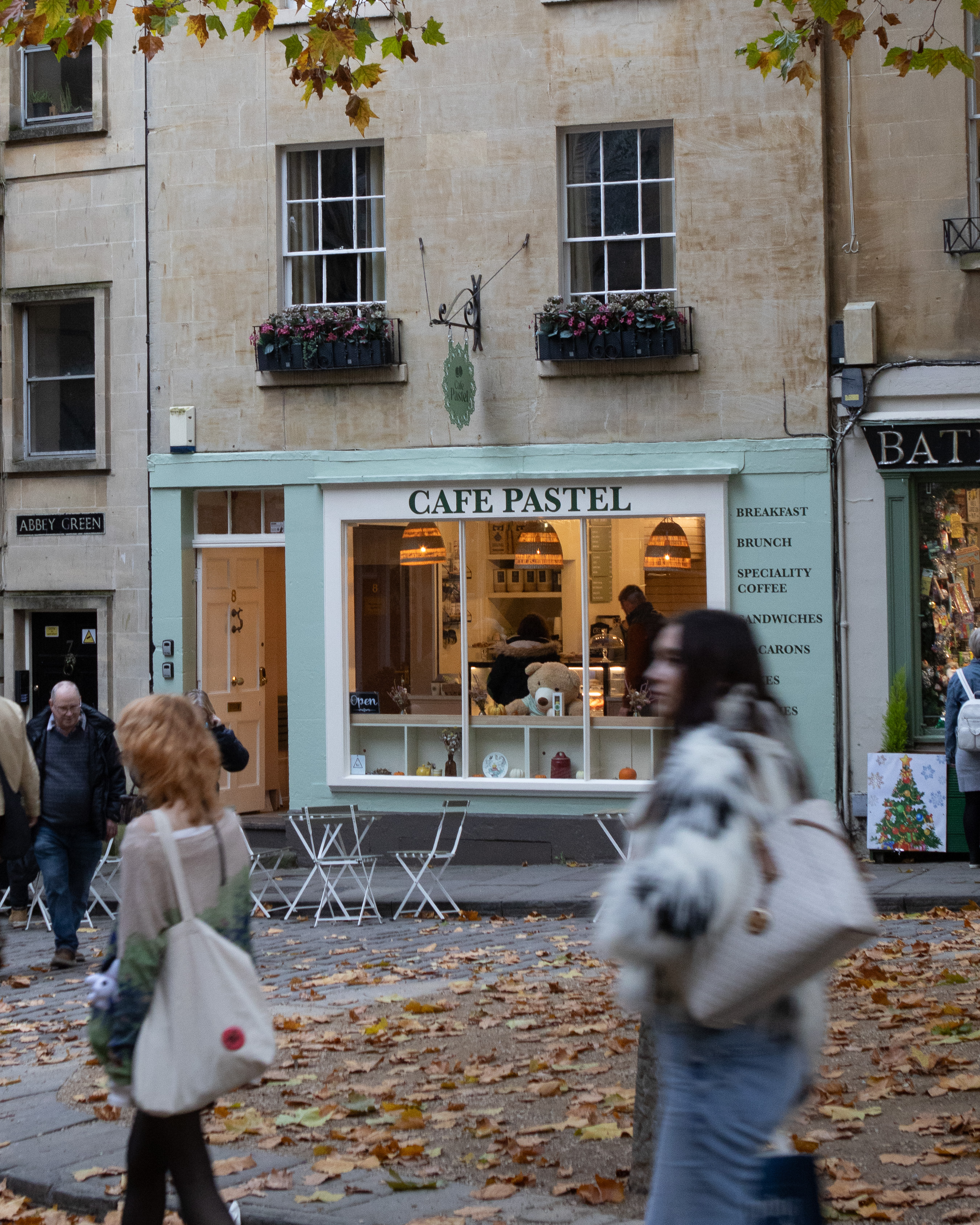 Pastel-green cafe shopfront on a leafy Bath cobblestone square in autumn
