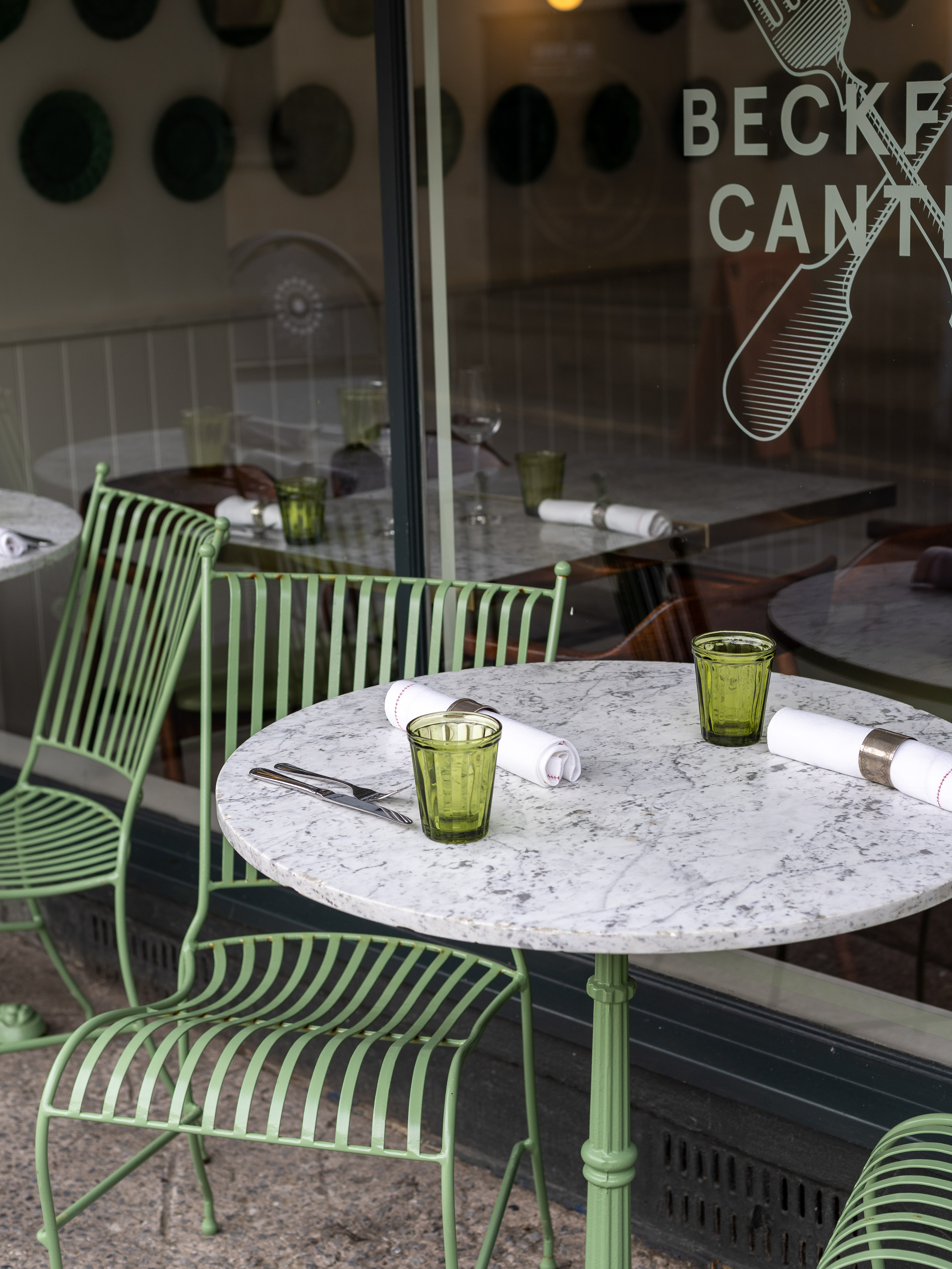 Marble-topped cafe table with green metal chair and tumblers beside a window etched with a comb logo