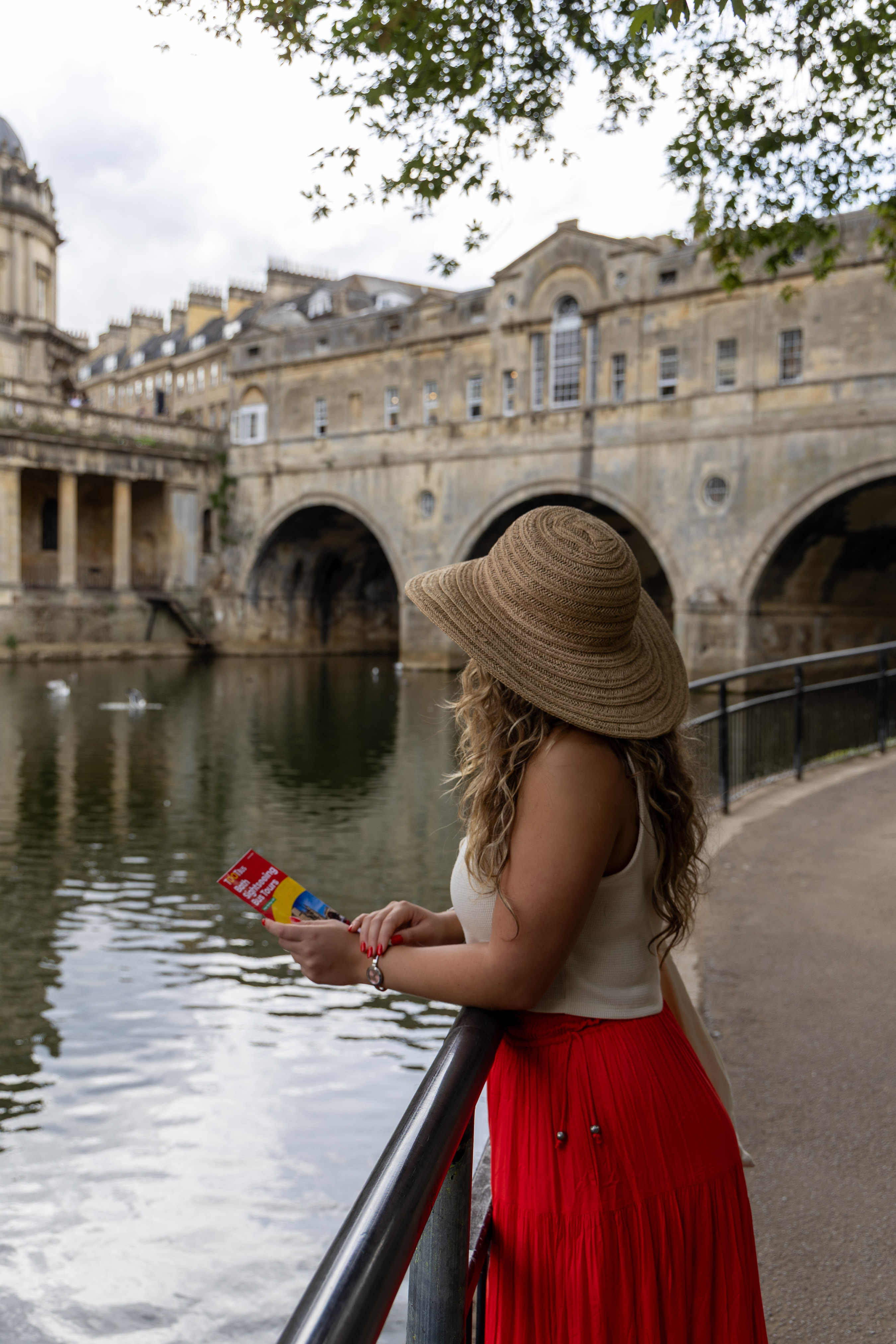Woman in a sun hat and red skirt looking out at Pulteney Bridge over the River Avon