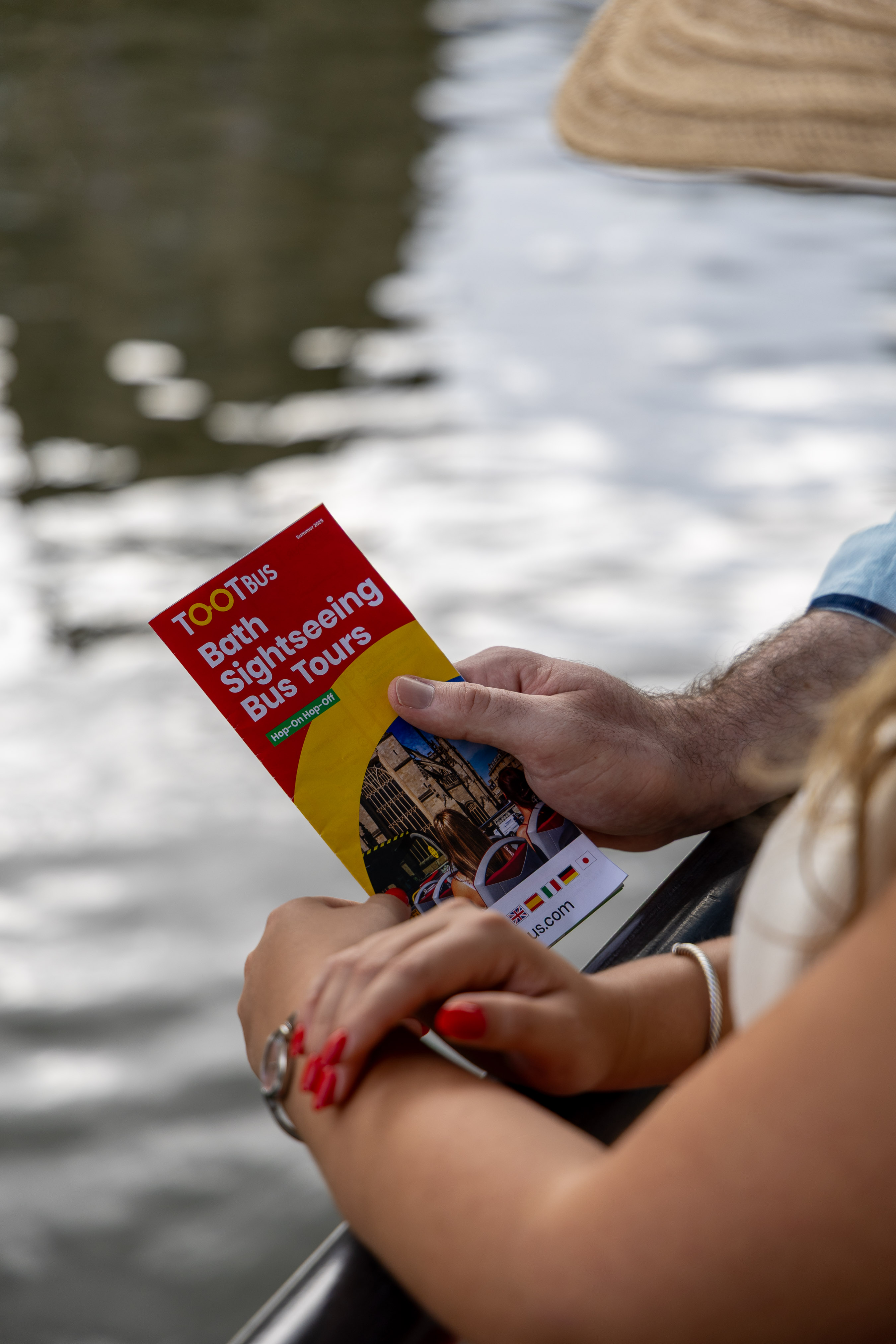 Open-top sightseeing bus brochure held above the River Avon by a passenger on the upper deck