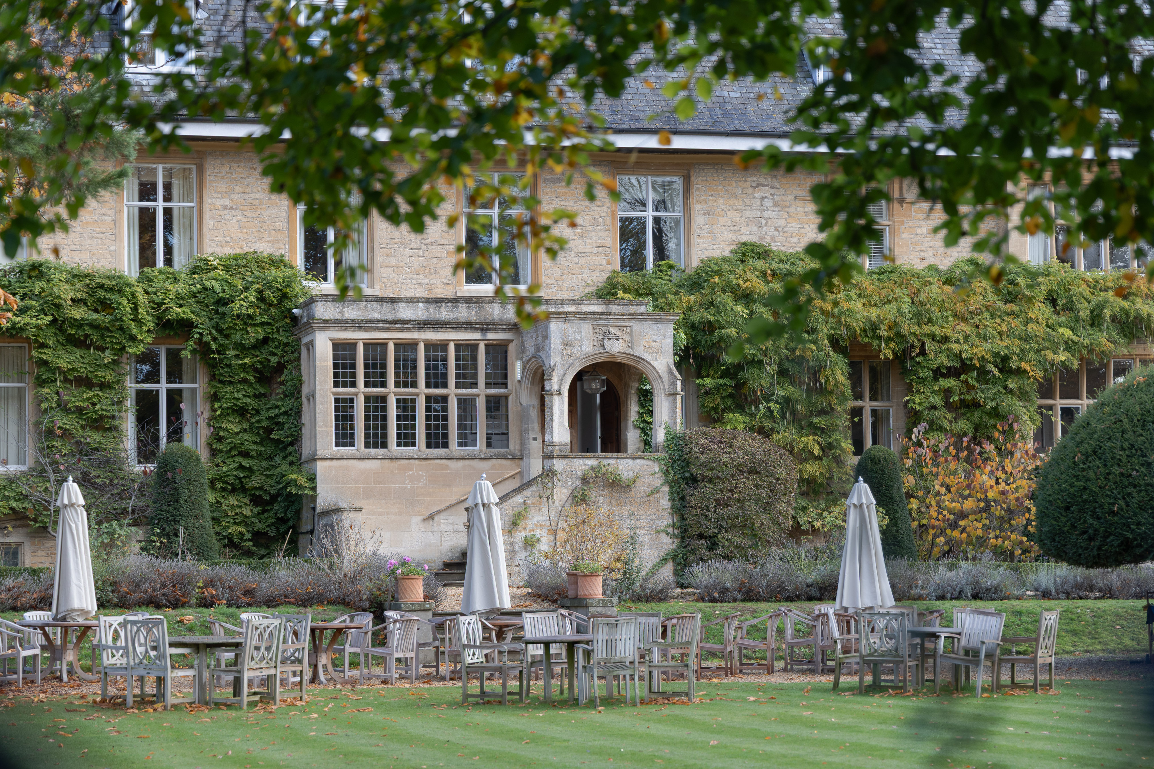 Lower Slaughter, Cotswold-stone country house with autumn creeper and a garden terrace of teak chairs and parasols