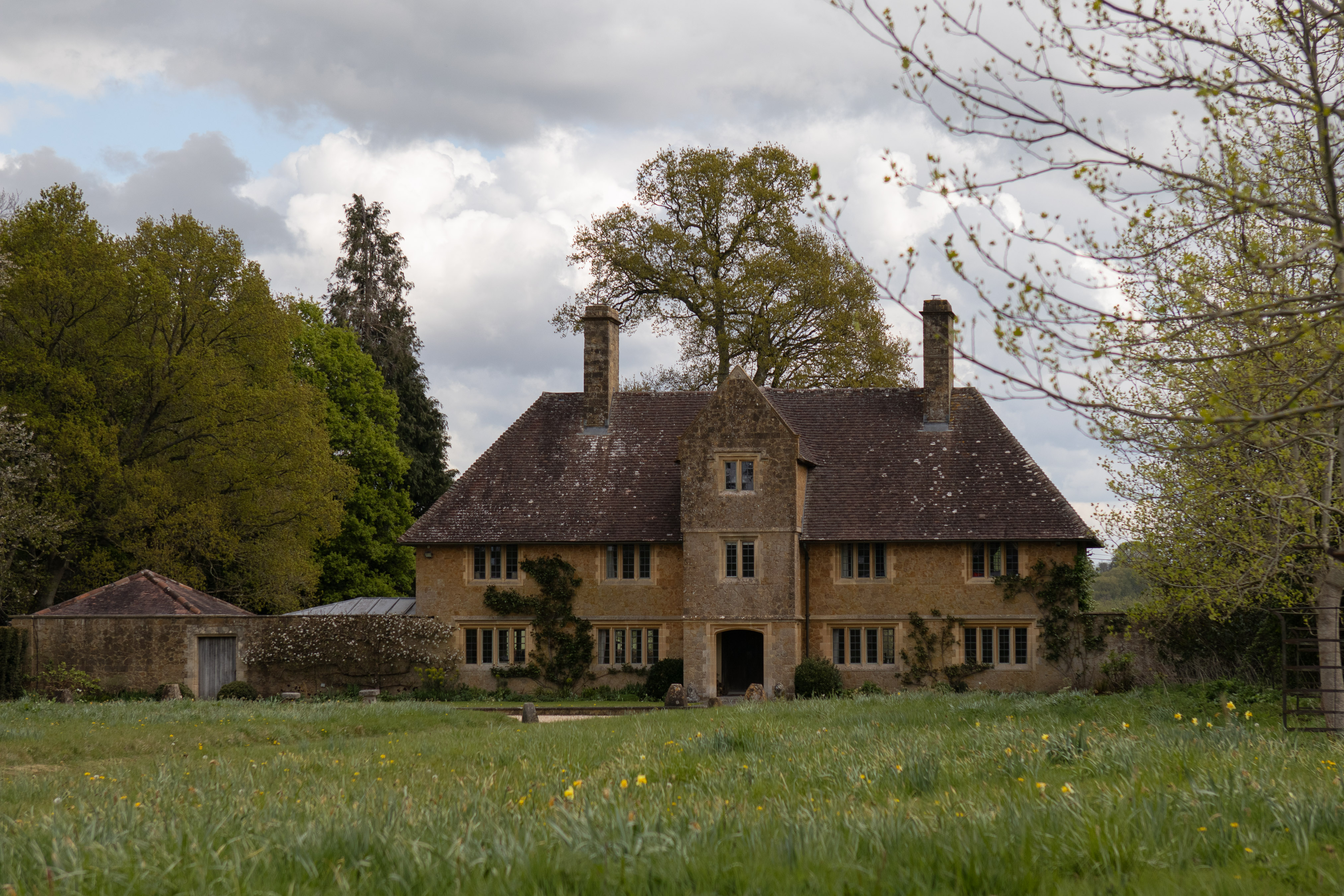 Barrington Court, honey-stone Jacobean manor house set across a wildflower meadow under spring skies