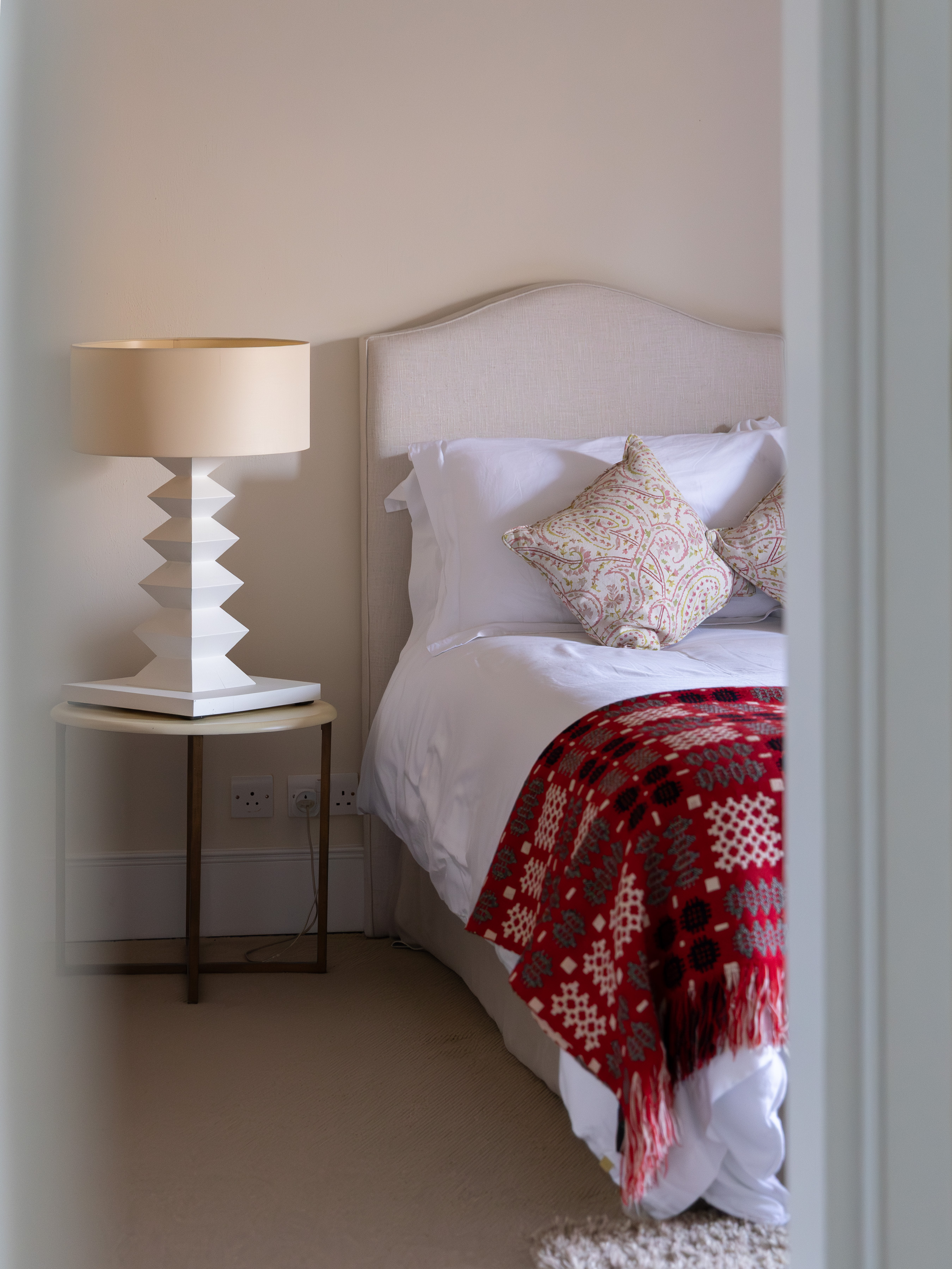 Cream upholstered headboard and crisp white bedding with a red and grey Welsh tapestry blanket folded across the foot of the bed