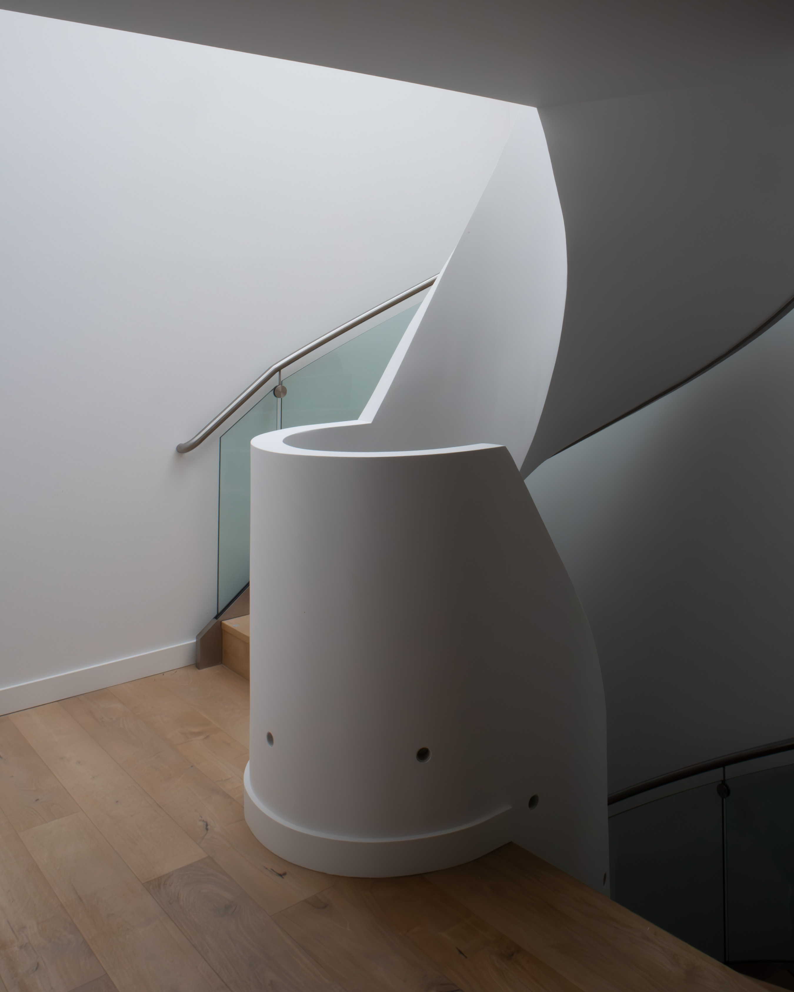 Sculptural curved white plaster staircase enclosure with brushed-metal handrail and oak flooring, contemporary architectural interior