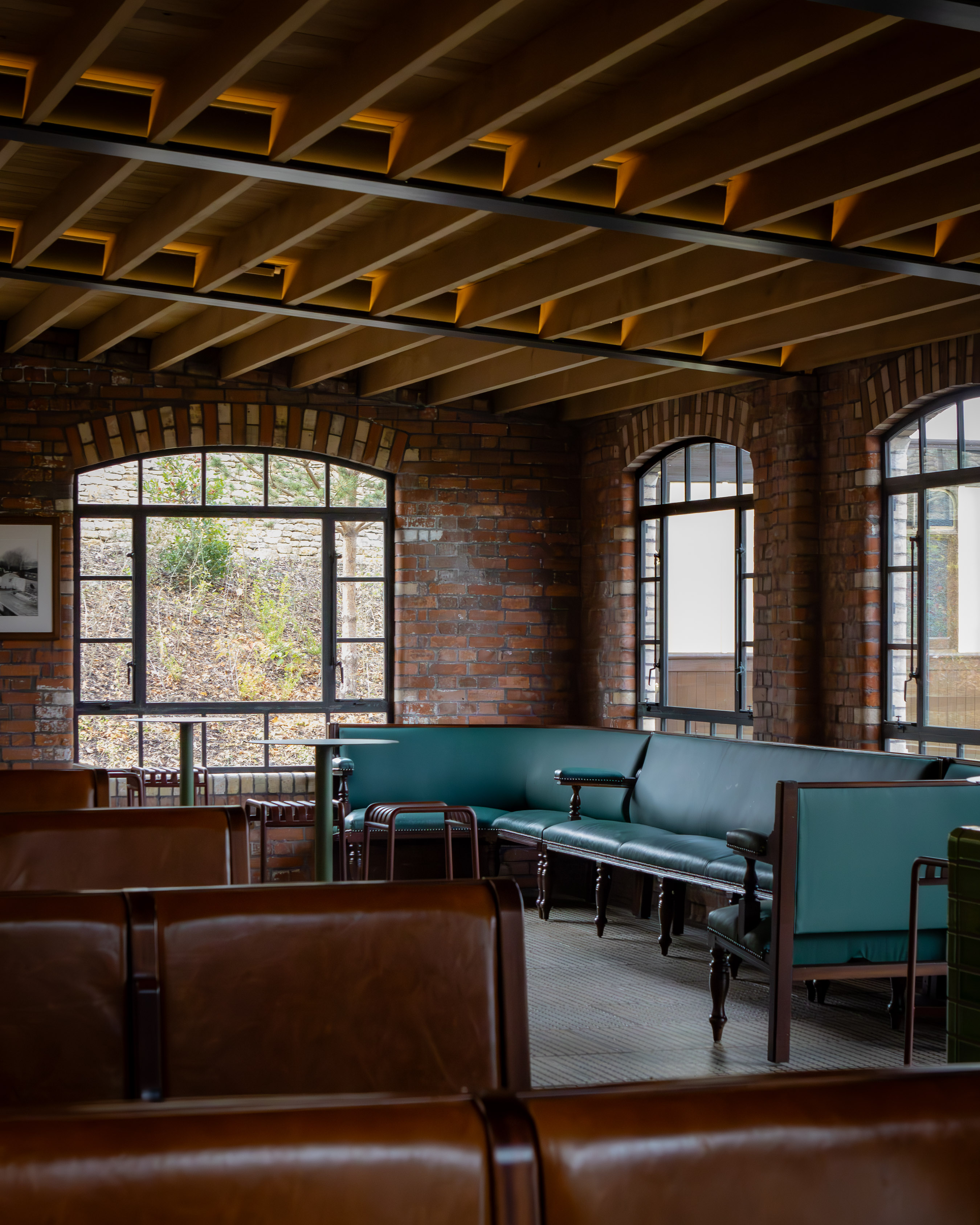 Restored Victorian industrial interior with exposed brick arches, timber beams and tan leather pub-style banquettes around the windows