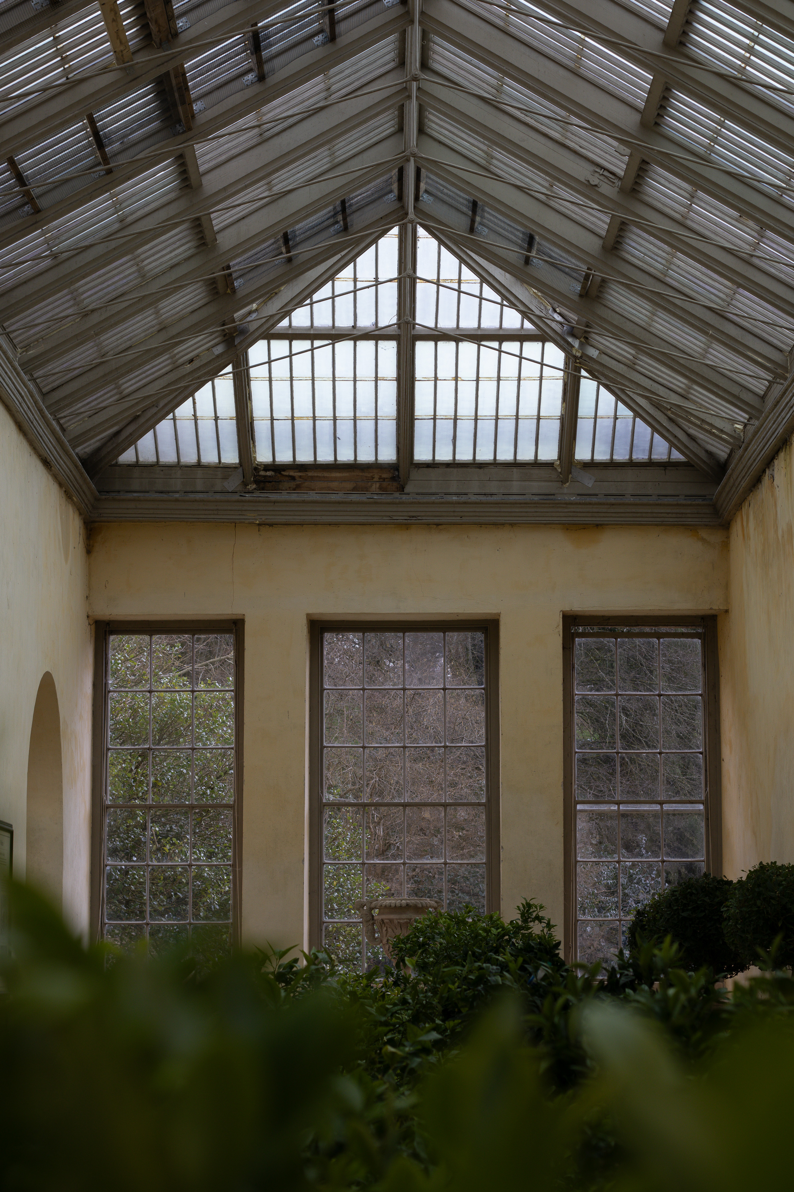 Dyrham Park, wrought-iron orangery roof framing tall arched windows, with potted greenery filling the foreground