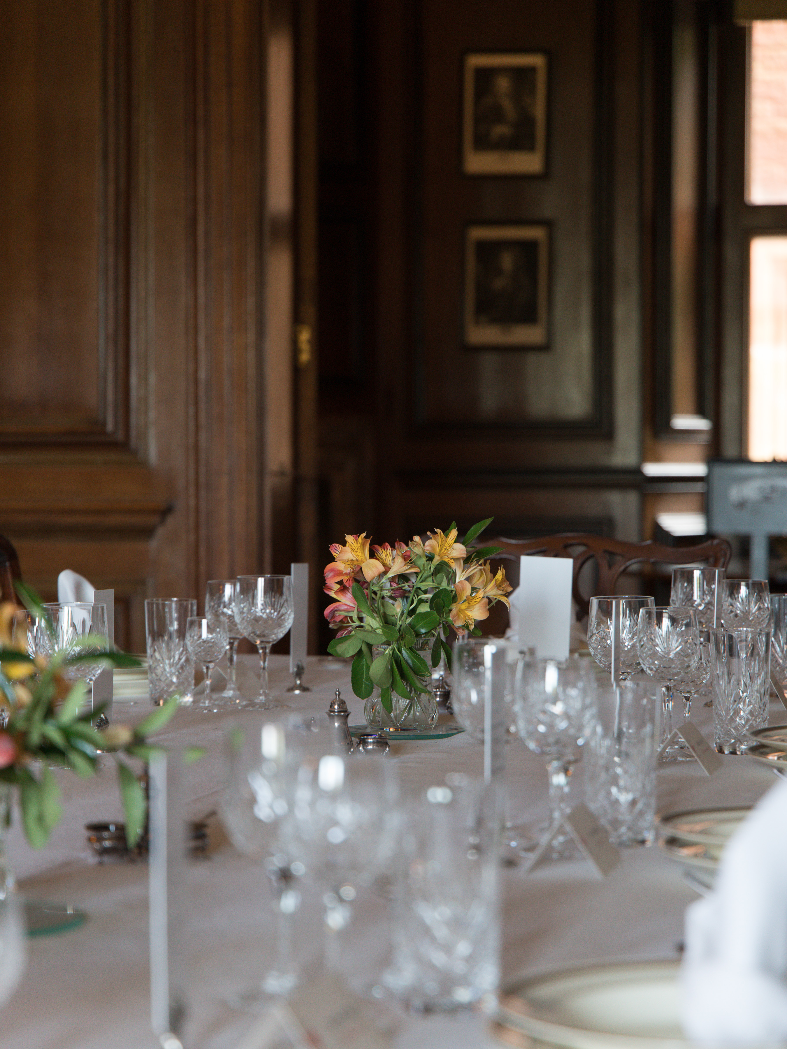 Dunster Castle, polished dining table set with cut crystal glasses, silver and fresh alstroemeria in a wood-panelled stately dining room