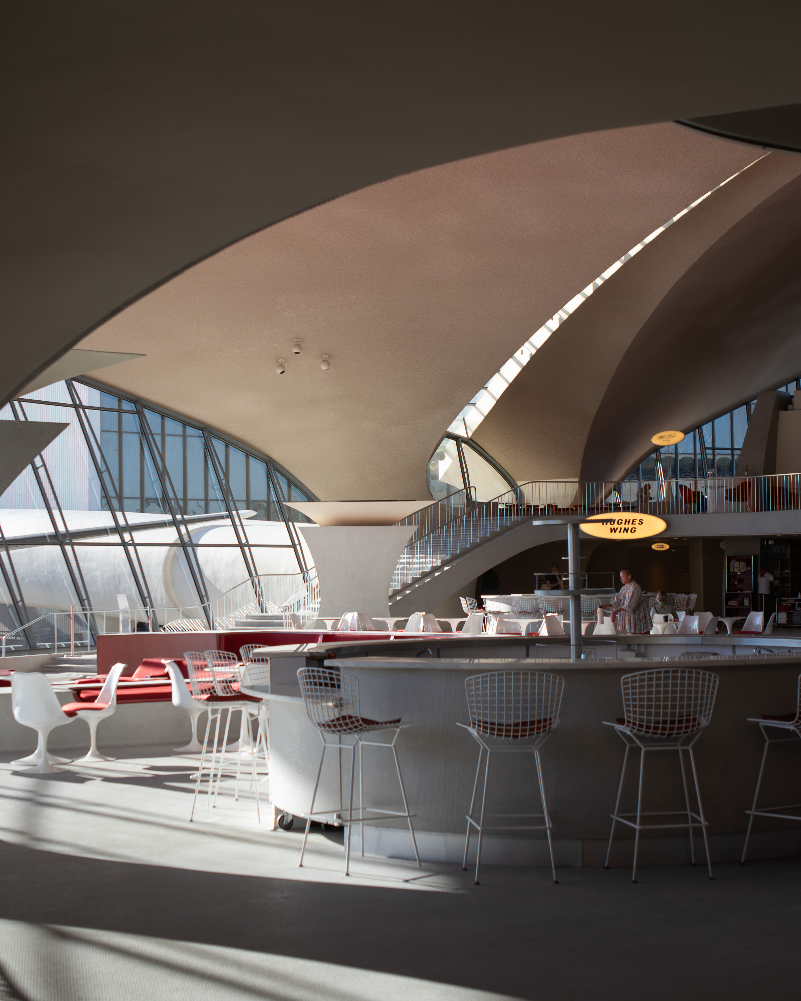 Sweeping vaulted concourse with Saarinen-style white tulip chairs, red carpet and curving cantilevered roof