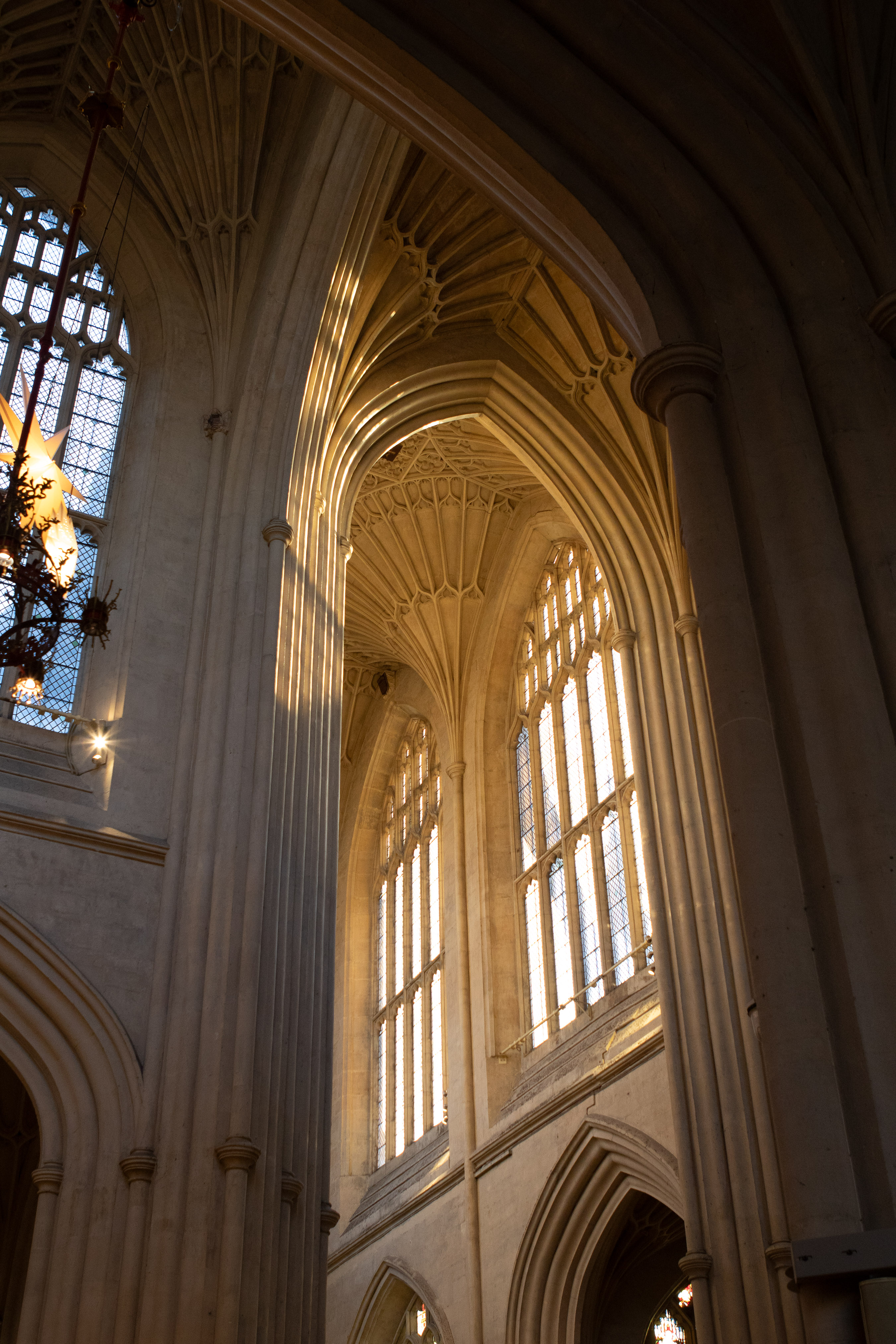 Bath Abbey, soaring Gothic fan-vaulted ceiling and tall stained-glass windows lit by golden sun inside a medieval cathedral