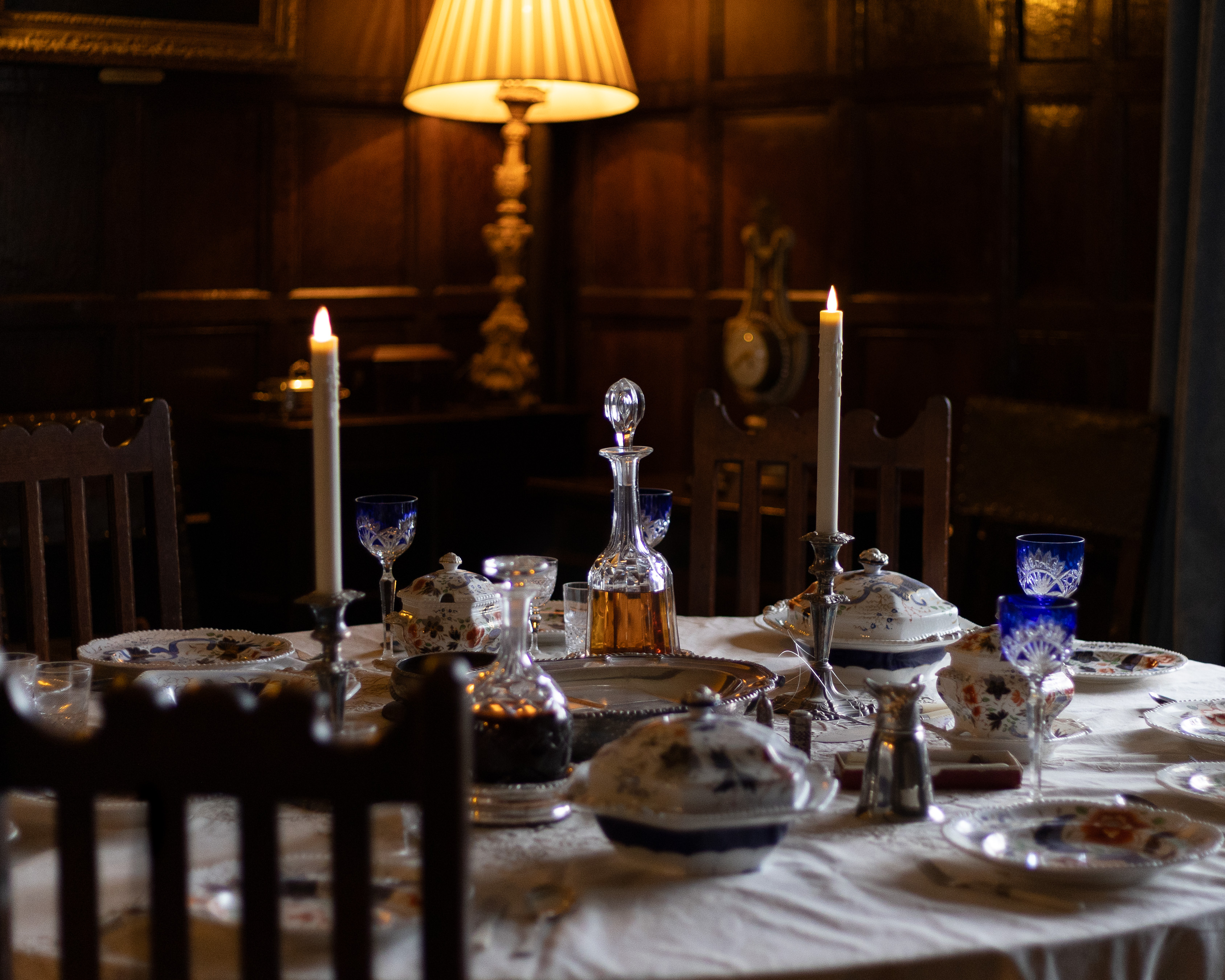Baddesley Clinton Manor, candlelit table laid with antique blue glass, silver tureens and decanters in a wood-panelled Jacobean dining room